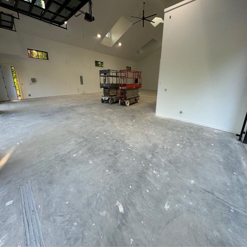 Spacious, unfinished interior with high ceilings, skylights, and a concrete floor. Two scissor lifts are parked, suggesting ongoing construction or renovation.