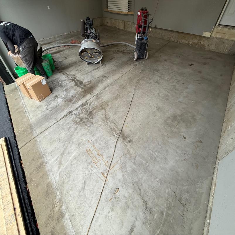 A person is working on a concrete floor in a garage, with equipment and boxes scattered around the area.