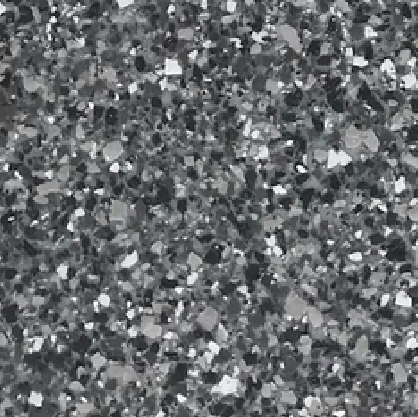 This image shows a close-up texture of rough, multi-toned gray asphalt with scattered small stones, creating a speckled pattern across the surface.